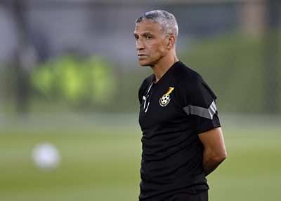 Chris Hughton stands with hands behind his back and looks thoughtful wearing a Ghana top on a training pitch