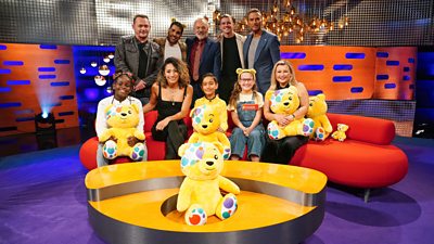 The celebrities and Graham Norton sit on and stand behind his red sofa, accompanied by children and Pudsey Bear soft toys. Standing: Perry Fenwick, Dr Ranj Singh, Graham Norton, Conor Gallagher and Matt Goss. Sitting: Karen Hauer, Rosie Ramsey and three children.