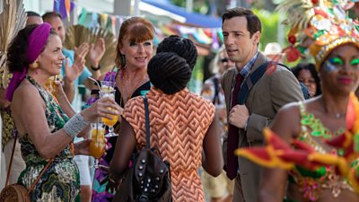 A scene from Death in Paradise 2023 Christmas episode featuring Elizabeth Bourgine, Doon Mackichan and Ralf Little speaking at a festival. 
