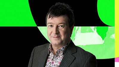 Headshot of Stuart Maconie in front of multi-coloured branding for 6 Music. 