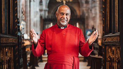 Very Revd Rogers Govender, Dean of Manchester Cathedral, stands with his hands outstretched at the doors of the cathedral