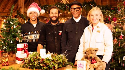 Will Kirk, Dominic Chinea, Jay Blades and Kirsten Ramsay stand in a very festive workshop, decorated with lights, wreaths and Christmas trees