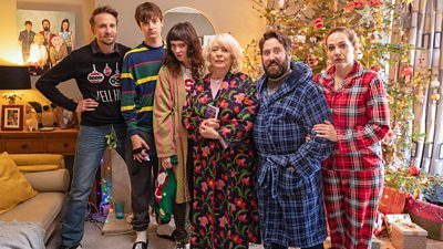 Robin (Tom Basden), Sam Jessop (Jude Collie), Amy Jessop (Freya Parks), Sue Jessop (Alison Steadman), Paul Jessop (Jim Howick), and Rachel Jessop (Katherine Parkinson) in pyjamas by a Christmas tree