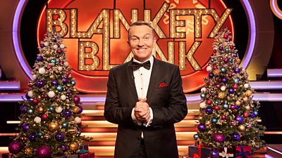 Bradley Walsh stands between two Christmas trees, smiling