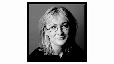 A black and white portrait image of Caroline Aherne. She smiles for the camera, wearing glasses.