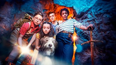 Characters George, Dick, Julian, Anne and Timmy the Dog looking down at camera in a cave. George has a rusted sword and Dick has a torch