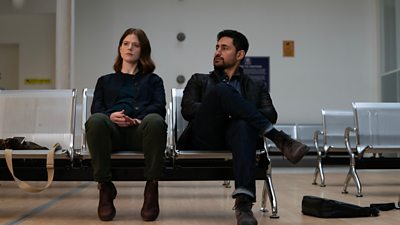 Kirsten Longacre (Rose Leslie) sits on a row of metal seats in a waiting area next to Daniel Ramsay (Amir El-Masry).  