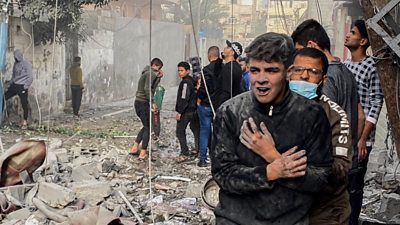 People stand around rubble, covered in dust