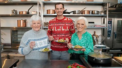 Shirley Erskine, Andy Murray and Mary Berry stand in a kitchen with plates of Mary's Kedgeree with Spinach and Herbs. Shirley and Andy wear Christmas jumpers. Shirley's is grey and blue with a band of festive snowflakes. Andy's is red and features llamas with the phrase 'fa la la la lama' written across it.