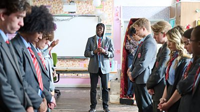 Inchez (Anthony J Abrahms) stands at the centre of a guard of honour, formed by his classmates, who all stand with their heads bowed