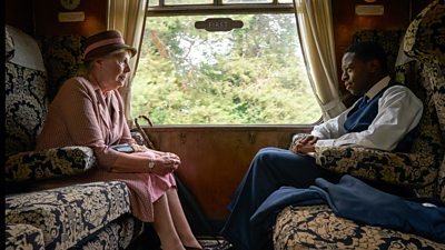 Miss Pinkerton and Luke Fitzwilliam sit opposite on another on a train 