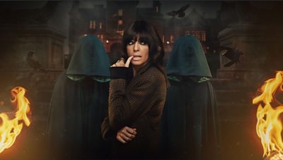 Claudia Winkleman stands between two Traitors in hooded green cloaks. Flames burn on either side of them while black birds fly in the background. The scene is set against the backdrop of a castle at night.