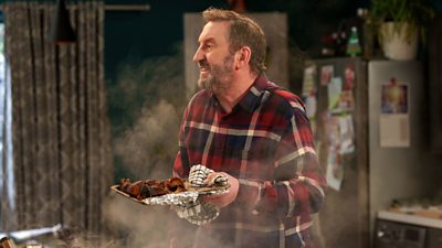 Lee Mack holding a tray of burnt food that's still smoking 