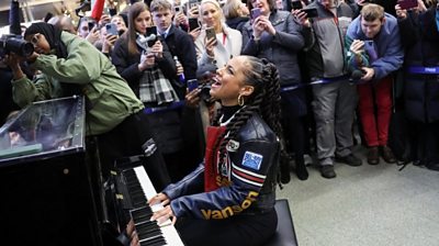 Alicia Keys sings and plays the piano in front of a crowd at London St Pancras station