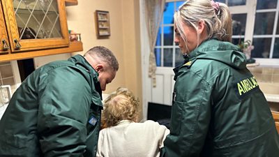 Two paramedics help an elderly woman off the floor