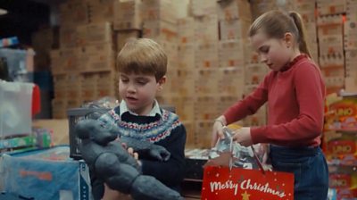 Prince Louis holding a gorilla toy and Princess Charlotte holding a bag saying 'Merry Christmas'