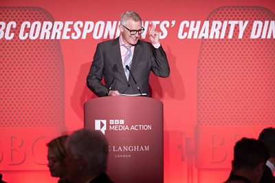 鶹Լ presenter Jeremy Vine stands at a red podium with 鶹Լ Media Action and The Langham London logos. The backdrop reads The 鶹Լ Correspondents' Charity Dinner.