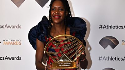 Faith Kipyegon in dress holds up athlete of the year trophy