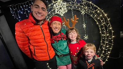 newsround presenter otis standing with zoe the elf and two kids in front of a ring of lights