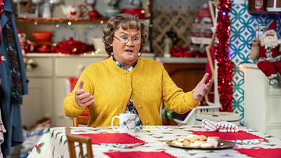 Brendan O'Carroll as Agnes Brown. Agnes sits at the kitchen table looking exasperated.