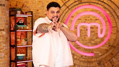 Big Has in the MasterChef kitchen smiling and pointing to the camera