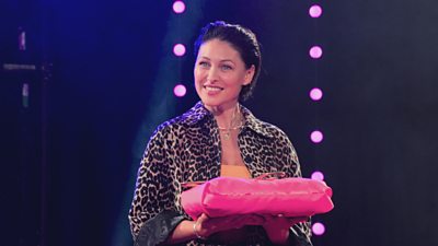 Emma Willis wearing a leopard print shirt holding a pink case and smiling