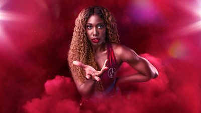 Fire stood against a red background, with one hand on their hip, and the other reaching out to the camera