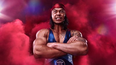 Viper stood against a red background with their arms folded 