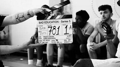 Black and white behind-the-scenes photo from the set of Bad Education series five featuring a clapperboard. 