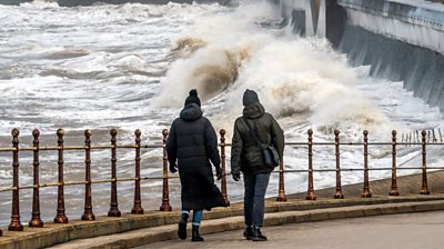 People walk near breaking waves on the sea front