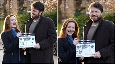 Behind the scenes, Cormoran Strike (Tom Burke) and Robin Ellacott (Holliday Grainger). They hold a clapperboard for the start of shoot and laugh.