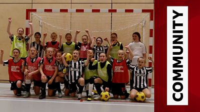 young girls in Newcastle kit cheer in front of indoor goalposts