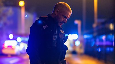 Martin Freeman as Chris in The Responder series 2. He stands, head bowed, looking at the ground at night. Behind him there are blurred vehicles and lights.