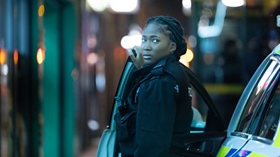 Adelayo Adedayo as Rachel. She emerges from a police car in uniform, looking back over her shoulder.