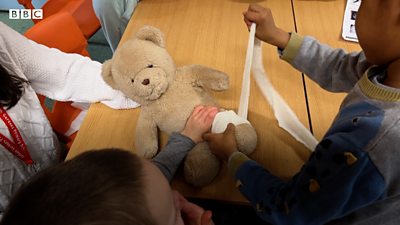 A boy putting a bandage on a teddy bear's leg