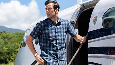 DI Neville Parker (Ralf Little) stands on the steps of a plane and looks back over his shoulder 