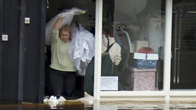 woman carrying wedding dresses out of flooded shop