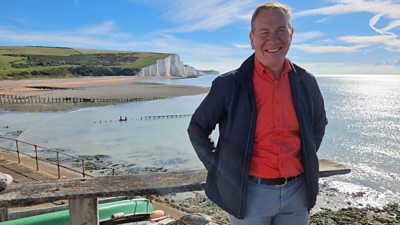 Michael Portillo with a beach and pier behind him