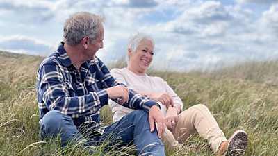 Robson sits on a grassy hill laughing with a woman