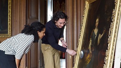 Two people point a torch at an old painting 