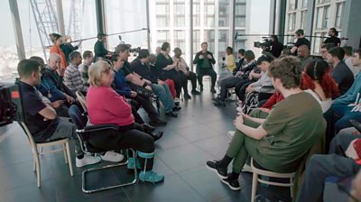 Michael Sheen sits alongside thirty-five interviewers in a large room. TV cameras and production staff film the group 