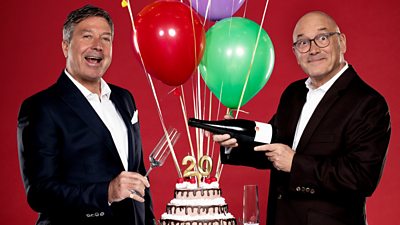 John Torode and Gregg Wallace smile to camera, stood either side of balloons and a grand cake with a "20" candle. Gregg tips a bottle to pour John a glass of wine