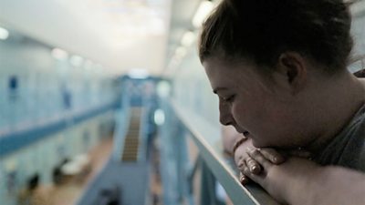 A woman rests her arms on a balcony overlooking a prison space