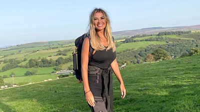 Christine McGuinness stands in a field with rolling hills behind her and smiles to camera 