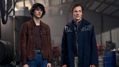 Bardon (Ben Rose) stands next to Eamonn (Peter MacDonald) in a warehouse