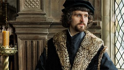 Harry Melling as Thomas Wriothesley stands in a grand wooden-panelled room and looks out a window 