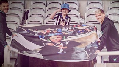Tyler standing proudly in St James' Park stands with the flag of himself