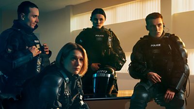 Characters Stevie, Grace, Annie and Tommy looking at something off screen wearing their police uniforms