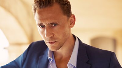 Headshot for Tom Hiddleston, wearing a blue suit and looking to camera. 