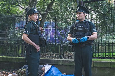 Two police officers stand in front of a homeless man